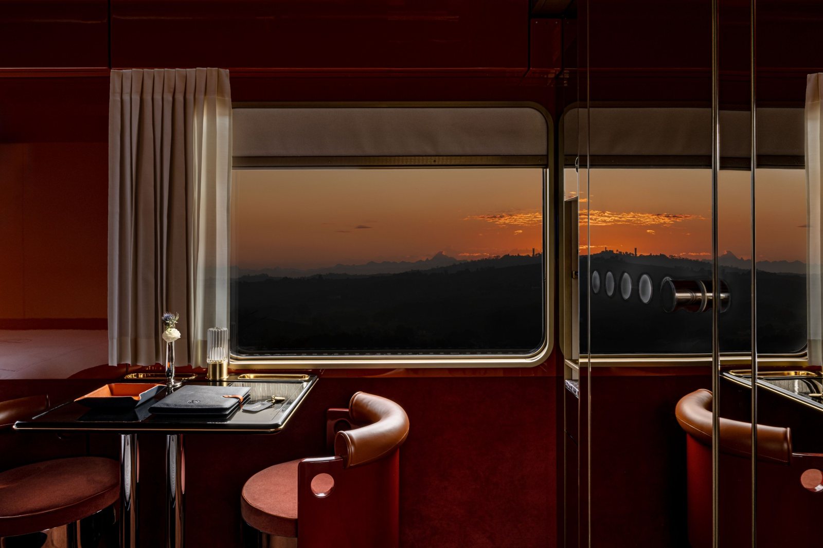 A cabin table and leather chair before a window at dusk over the Italian hills