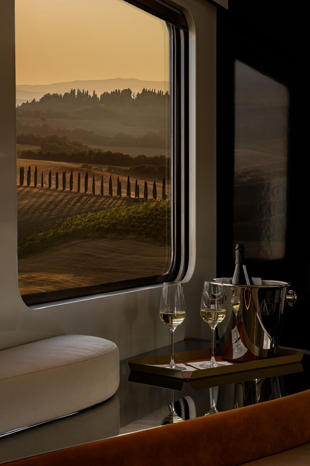 Two glasses of Champagne and an ice bucket beside a window over golden Tuscan hills