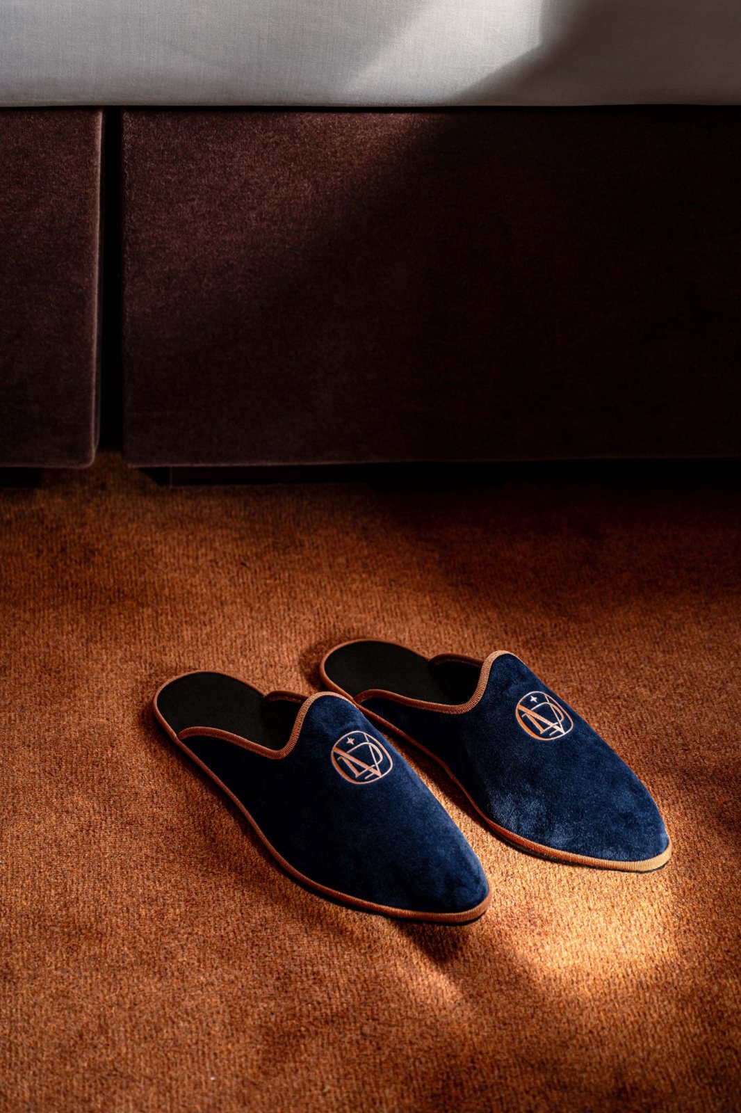 Navy velvet slippers embroidered with the La Dolce Vita monogram beside the bed