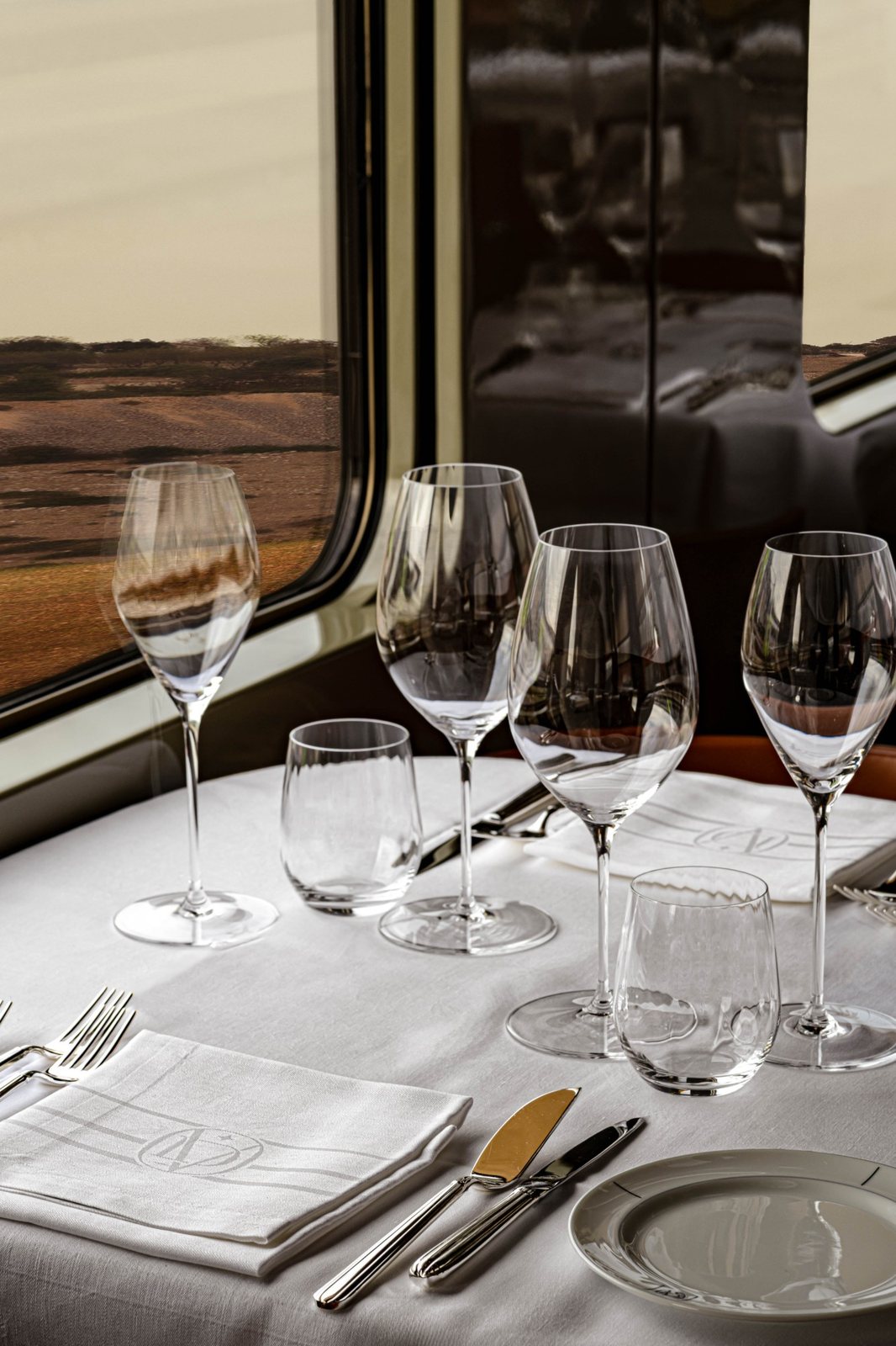 A table set with crystal glasses and monogrammed linen beside a train window