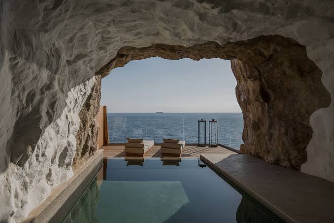 A cave-cut swimming pool opening onto the open sea, loungers on the deck beyond