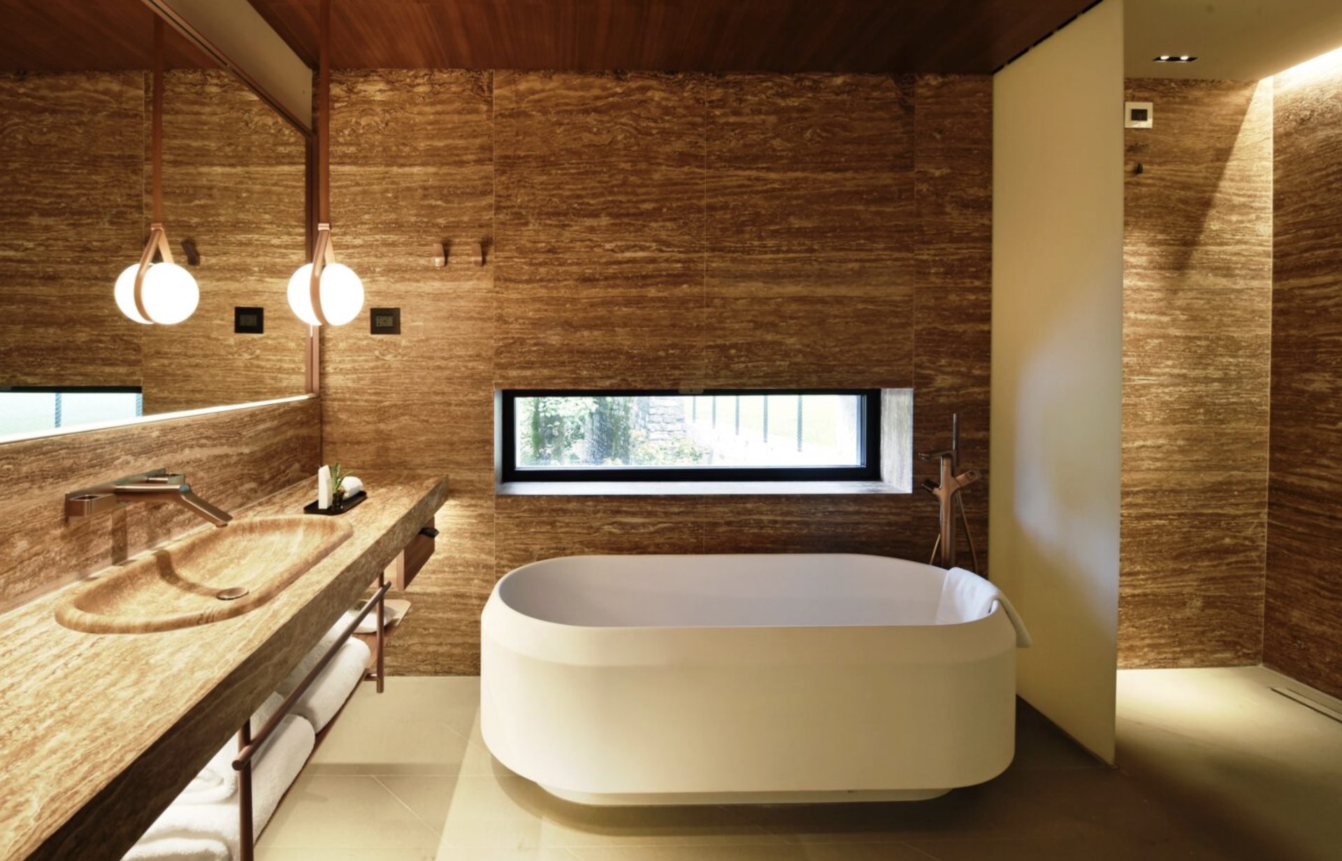 An Il Sereno bathroom with travertine walls and a sculpted soaking tub