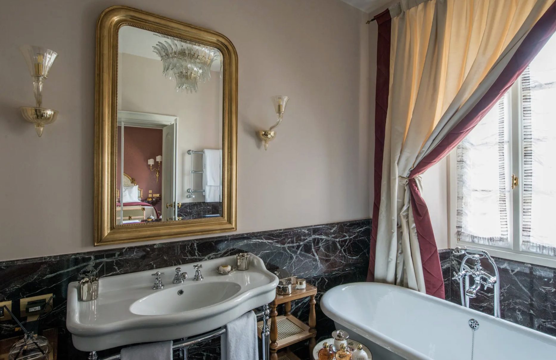 A Passalacqua bathroom with a gilt mirror, glass sconces and dark marble