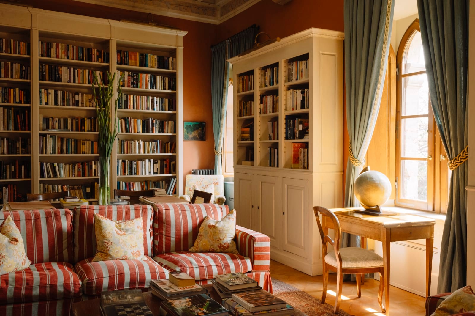 The library at Borgo Pignano, with bookshelves, striped sofas and a globe by the window