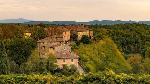 The stone houses of the Il Borro borgo at golden hour above the Tuscan woods