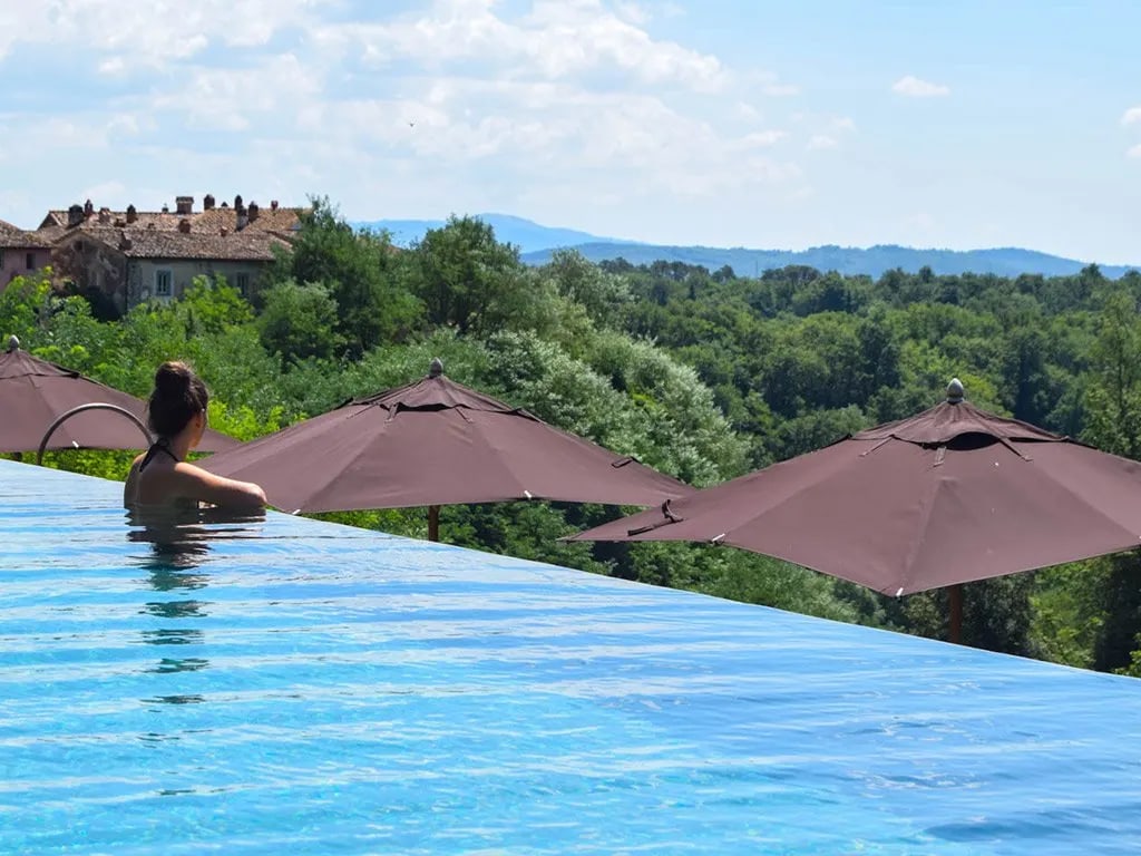 A guest in the infinity pool at Il Borro, looking over the woods to the medieval borgo and the hills